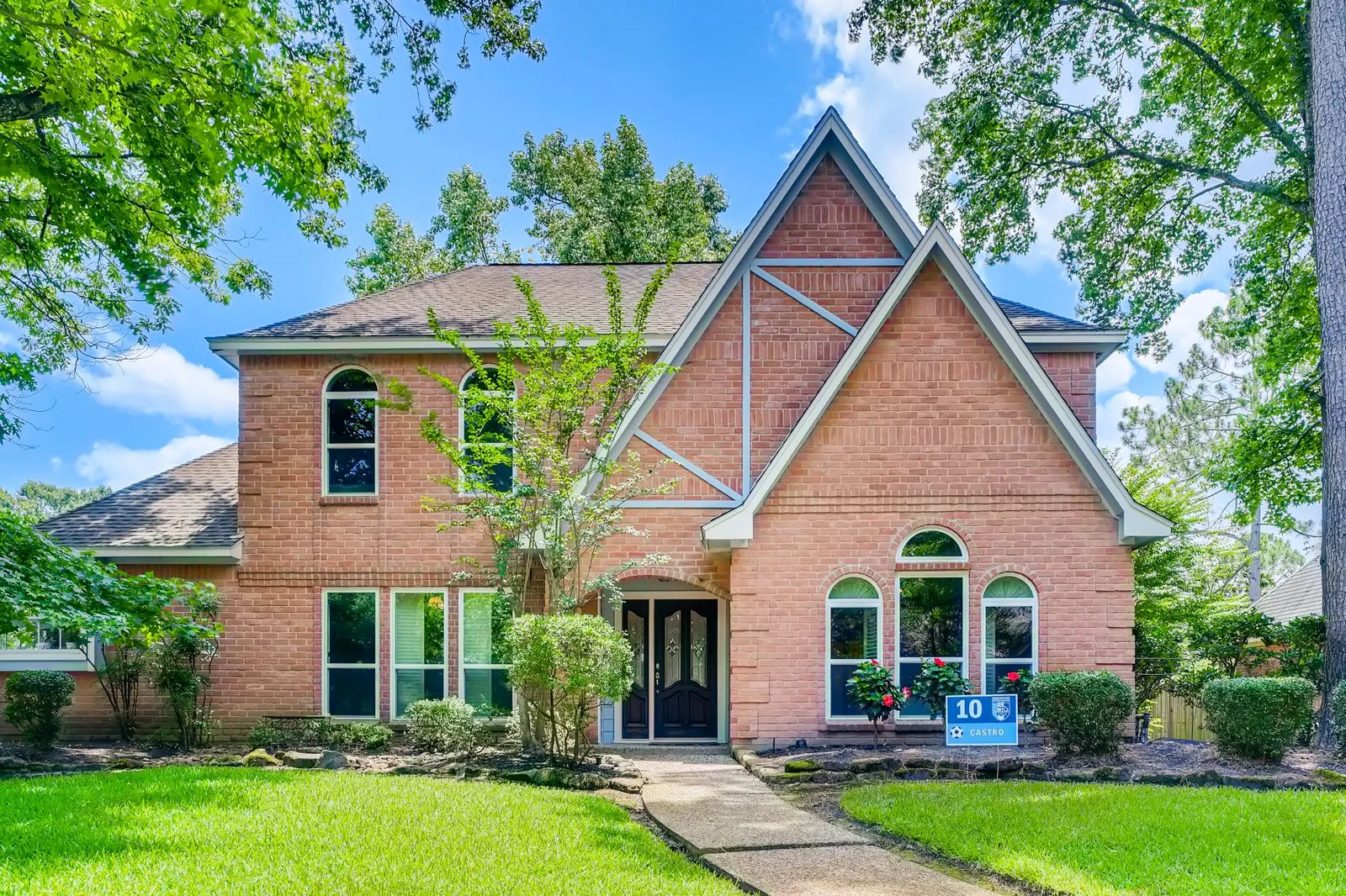 Two-story brick house with lush front yard, trees, and striking architecture.